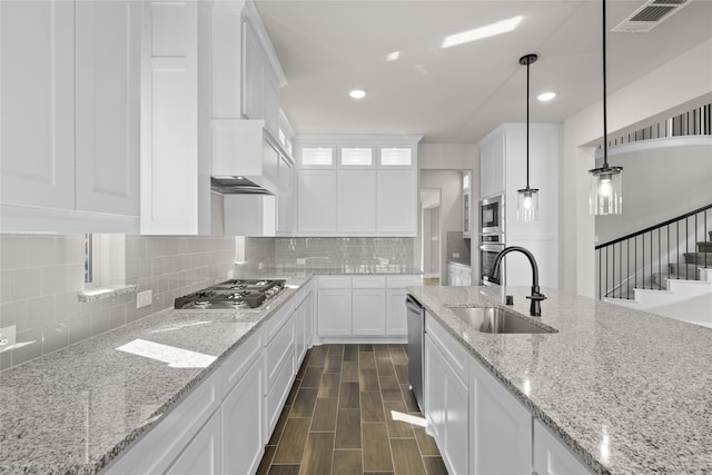 kitchen with white cabinetry, stainless steel appliances, decorative light fixtures, light stone counters, and sink