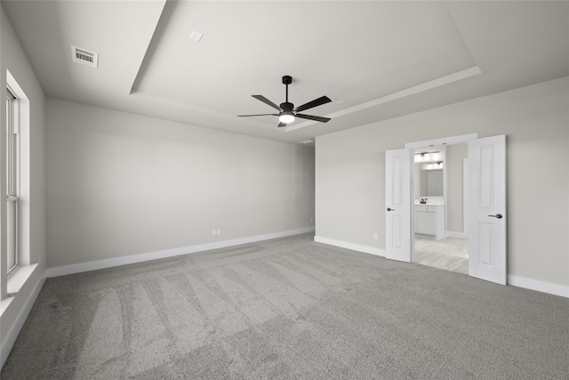 unfurnished bedroom with ceiling fan, light carpet, multiple windows, and a tray ceiling