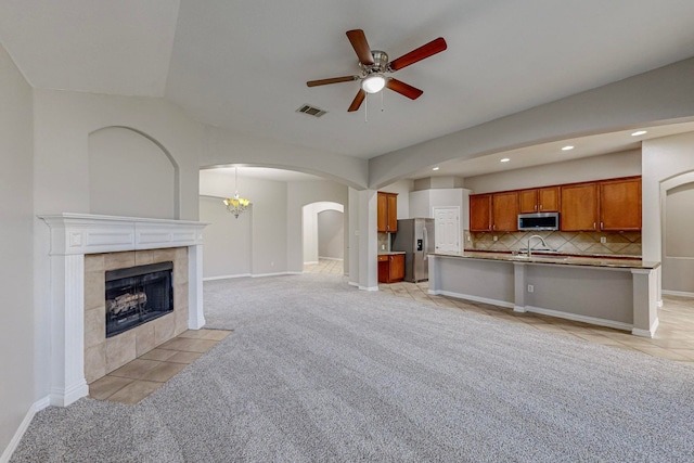 unfurnished living room with lofted ceiling, ceiling fan with notable chandelier, a tile fireplace, and light carpet