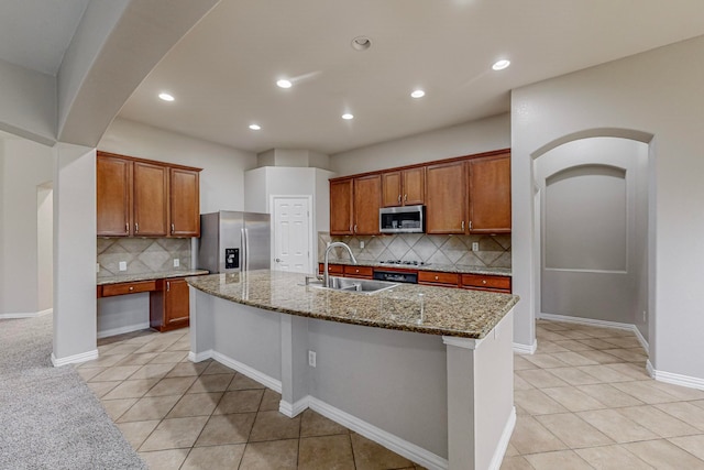 kitchen with dark stone countertops, backsplash, appliances with stainless steel finishes, sink, and an island with sink