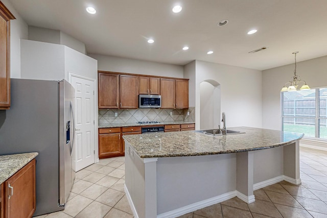 kitchen with a notable chandelier, an island with sink, light stone countertops, sink, and appliances with stainless steel finishes