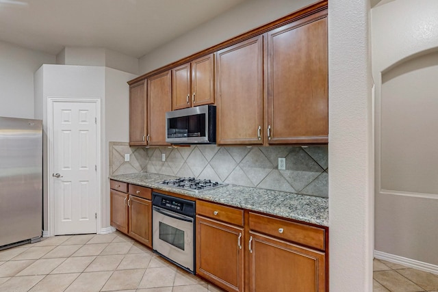 kitchen with appliances with stainless steel finishes, light stone counters, backsplash, and light tile patterned flooring