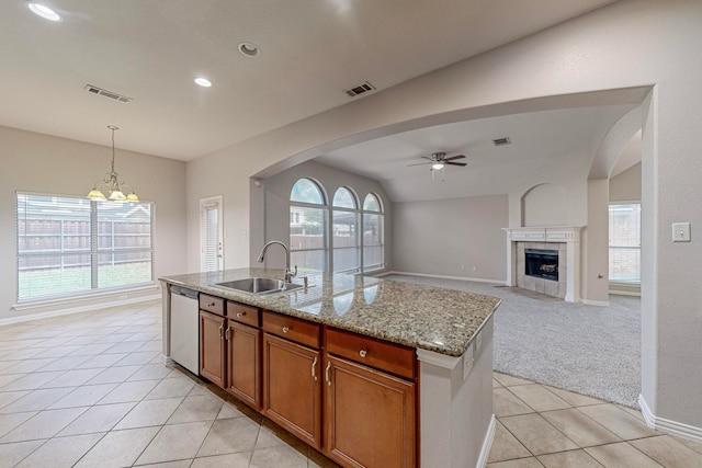 kitchen with light stone countertops, ceiling fan with notable chandelier, a fireplace, a kitchen island with sink, and sink