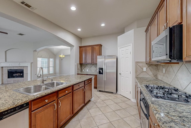 kitchen featuring a tiled fireplace, pendant lighting, backsplash, stainless steel appliances, and sink