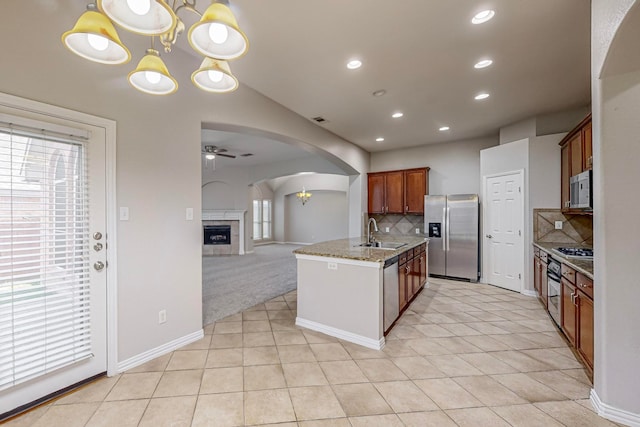 kitchen with pendant lighting, ceiling fan with notable chandelier, stainless steel appliances, light stone counters, and sink