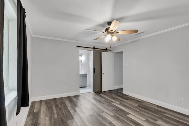 empty room featuring ornamental molding, dark wood-type flooring, ceiling fan, and a barn door