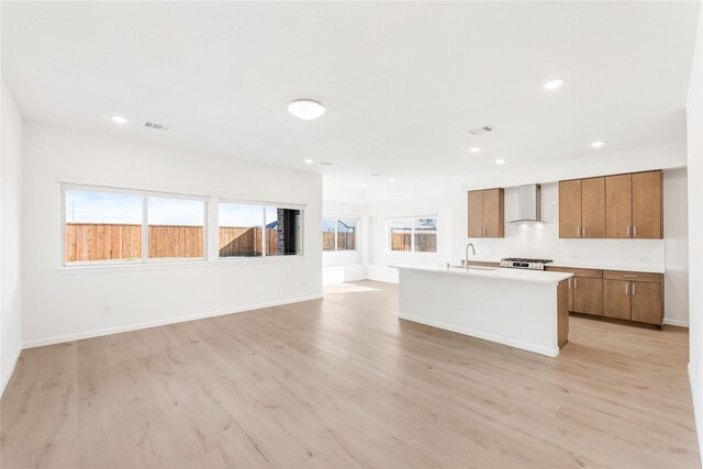 kitchen with gas range, sink, light hardwood / wood-style flooring, an island with sink, and wall chimney exhaust hood