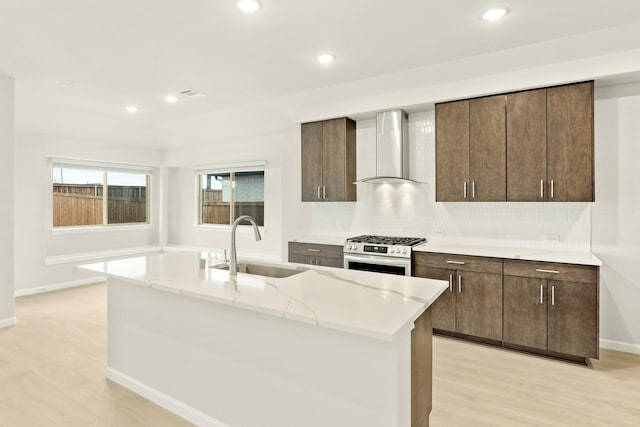 kitchen featuring hardwood / wood-style floors, appliances with stainless steel finishes, wall chimney range hood, an island with sink, and tasteful backsplash