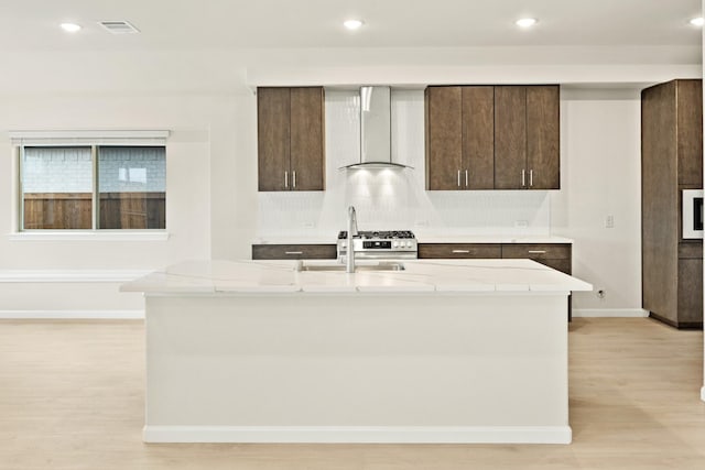 kitchen featuring stainless steel appliances, light hardwood / wood-style floors, sink, wall chimney exhaust hood, and a kitchen island with sink