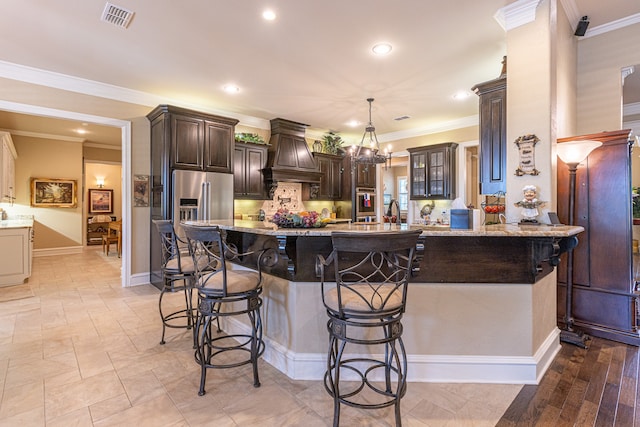 kitchen with a kitchen breakfast bar, custom range hood, ornamental molding, a chandelier, and light stone counters