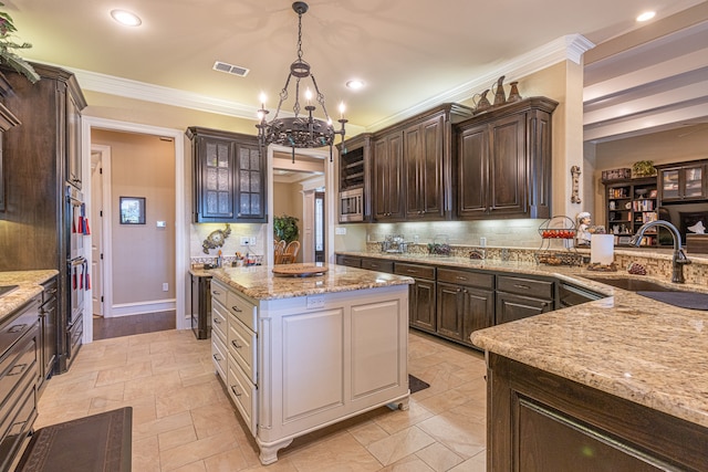 kitchen with a notable chandelier, light stone counters, a kitchen island, sink, and dark brown cabinetry