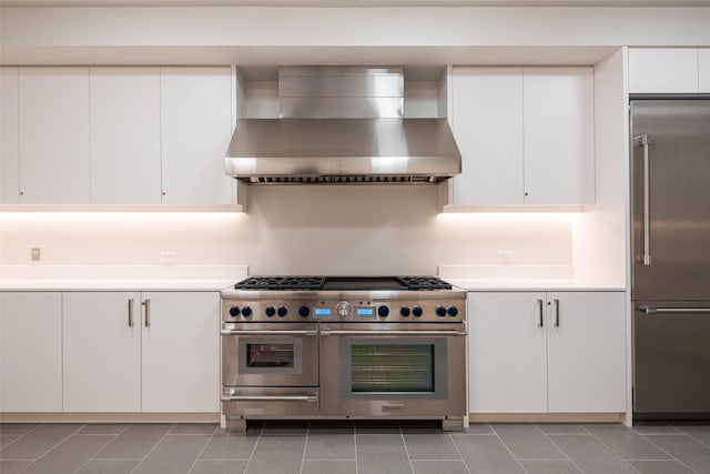 kitchen with wall chimney range hood, white cabinetry, and high quality appliances