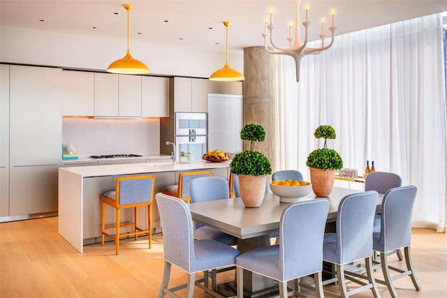 dining space featuring sink, a healthy amount of sunlight, an inviting chandelier, and light hardwood / wood-style flooring