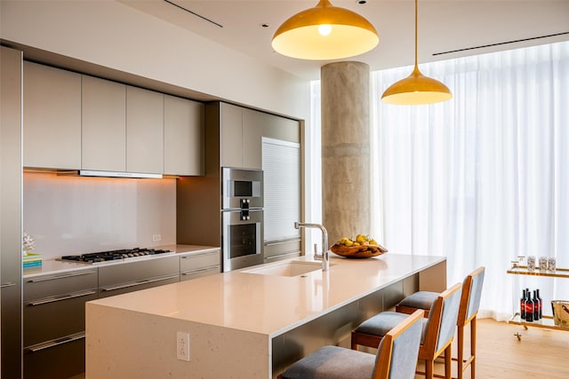 kitchen with pendant lighting, gas cooktop, an island with sink, sink, and light hardwood / wood-style floors