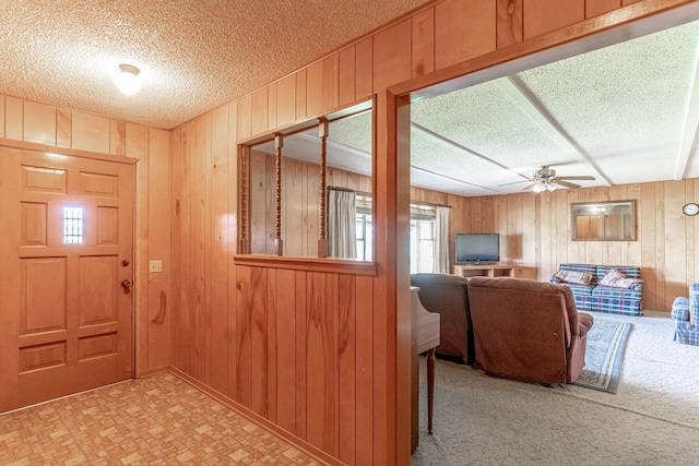 foyer entrance with ceiling fan, wooden walls, and a textured ceiling