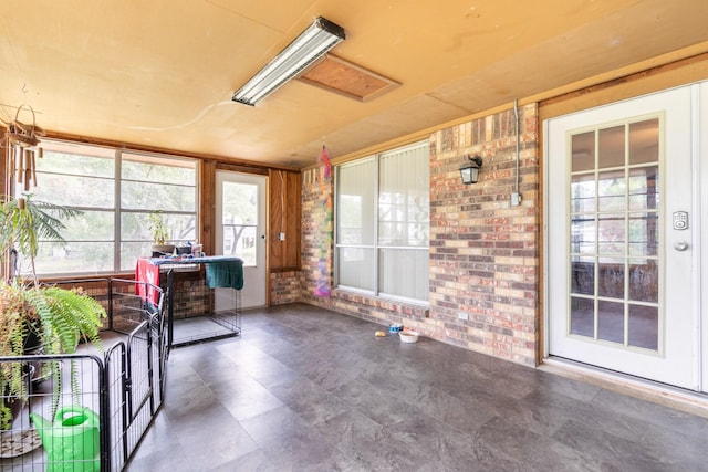 sunroom featuring attic access and brick wall