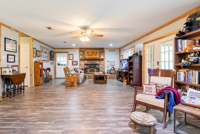 living room with a fireplace, ornamental molding, a textured ceiling, wood-type flooring, and ceiling fan