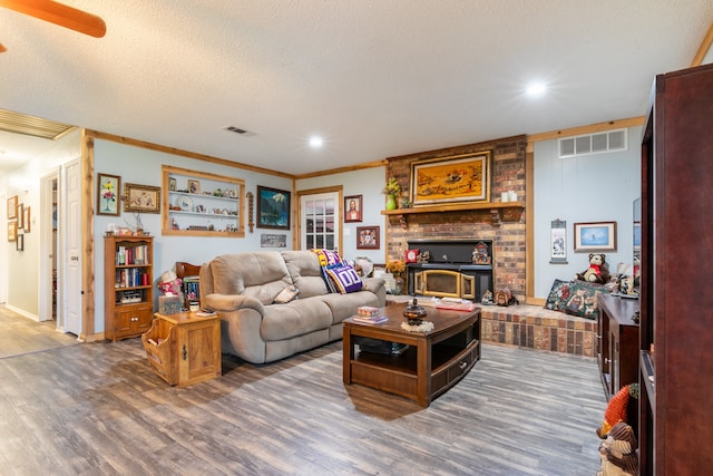 living room with crown molding, a brick fireplace, hardwood / wood-style floors, ceiling fan, and a textured ceiling