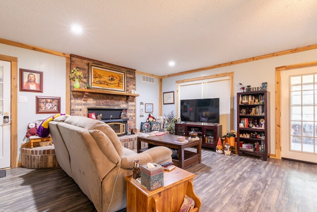 living room with a textured ceiling, ornamental molding, dark hardwood / wood-style floors, and a brick fireplace