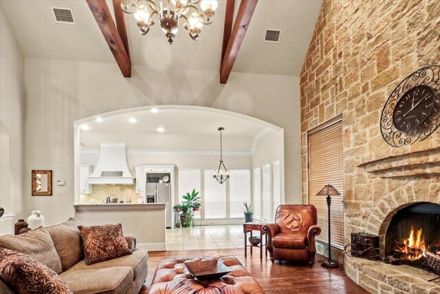 living room featuring a high ceiling, beam ceiling, an inviting chandelier, hardwood / wood-style floors, and a stone fireplace