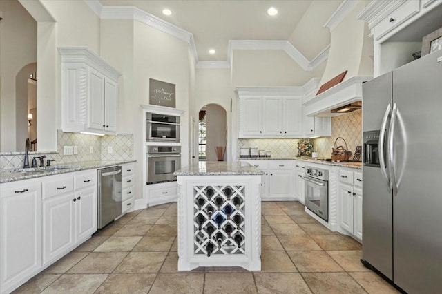 kitchen featuring a towering ceiling, custom exhaust hood, stainless steel appliances, white cabinets, and a kitchen island