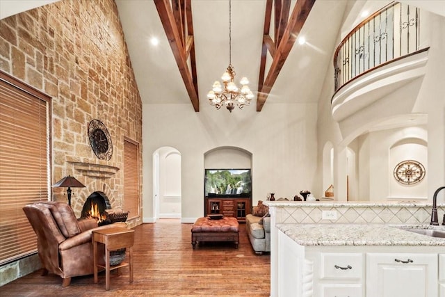 living room featuring high vaulted ceiling, sink, a fireplace, a notable chandelier, and beam ceiling