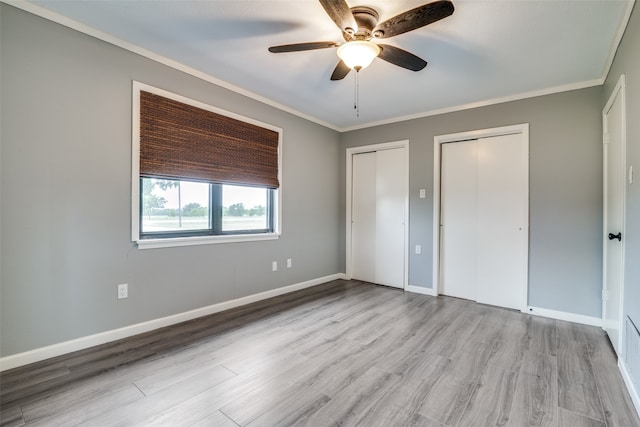 unfurnished bedroom featuring light wood-type flooring, ornamental molding, two closets, and ceiling fan