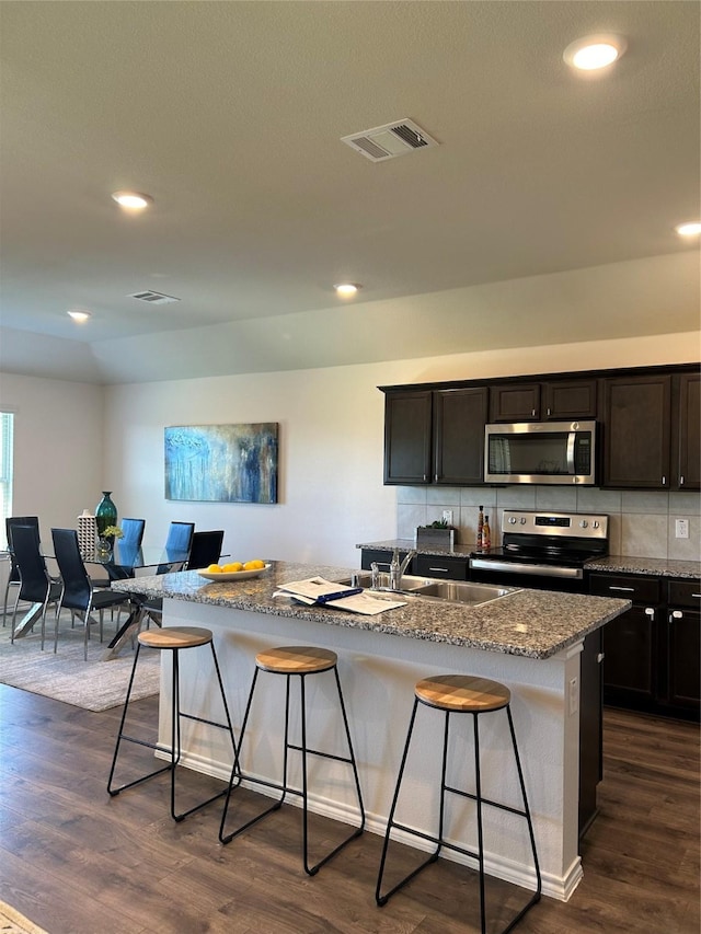 kitchen with dark wood-type flooring, a center island with sink, sink, a breakfast bar area, and stainless steel appliances