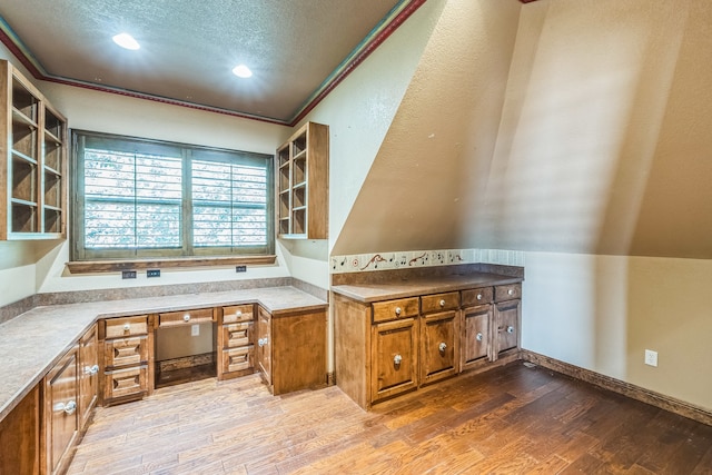 kitchen featuring hardwood / wood-style floors, built in desk, ornamental molding, and a textured ceiling