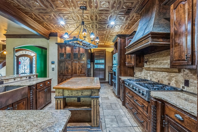 kitchen with an inviting chandelier, light stone counters, custom exhaust hood, stainless steel appliances, and a kitchen island