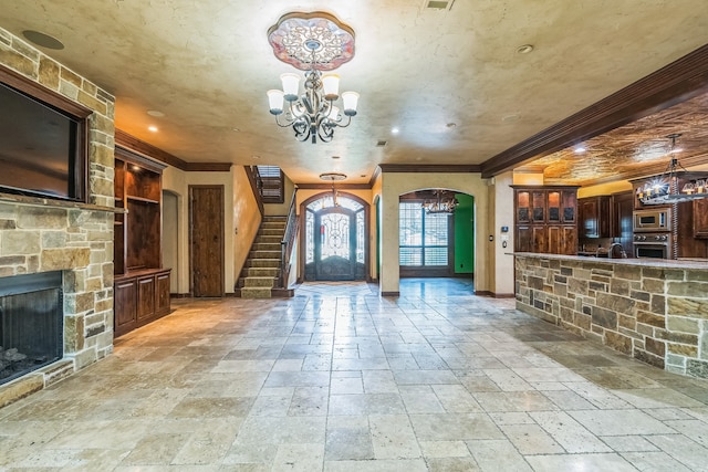 unfurnished living room with an inviting chandelier, crown molding, and a stone fireplace