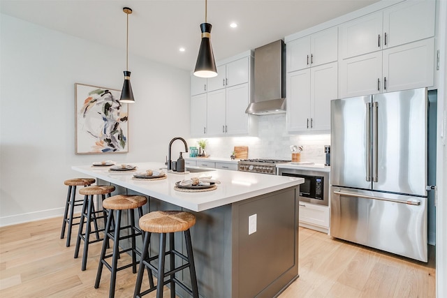 kitchen with wall chimney exhaust hood, light hardwood / wood-style flooring, stainless steel appliances, and a center island with sink