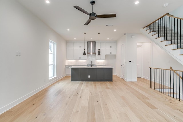 kitchen with white cabinets, ceiling fan, a center island with sink, and light hardwood / wood-style flooring