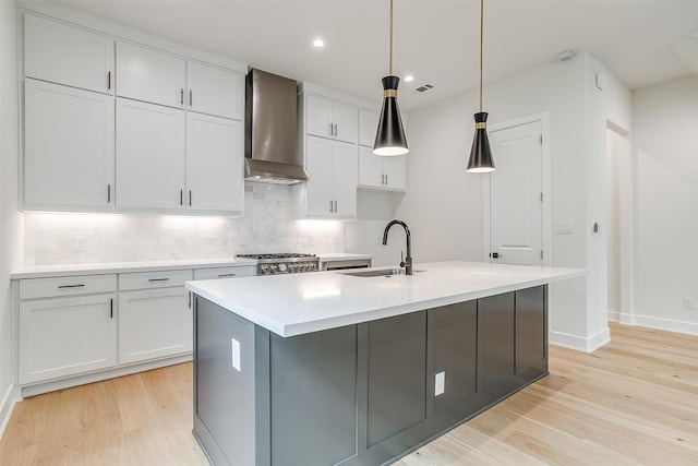 kitchen featuring hanging light fixtures, light hardwood / wood-style floors, sink, wall chimney exhaust hood, and a center island with sink