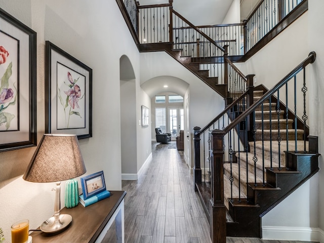 foyer with arched walkways, a towering ceiling, baseboards, and wood finished floors