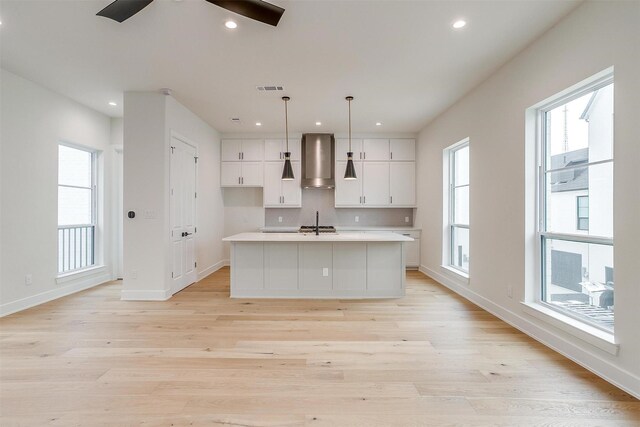 kitchen featuring a center island with sink, light hardwood / wood-style flooring, ceiling fan, and wall chimney exhaust hood