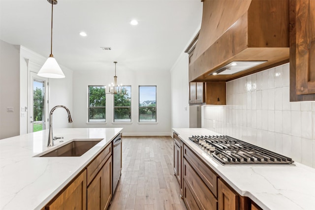 kitchen with premium range hood, appliances with stainless steel finishes, pendant lighting, sink, and light stone countertops