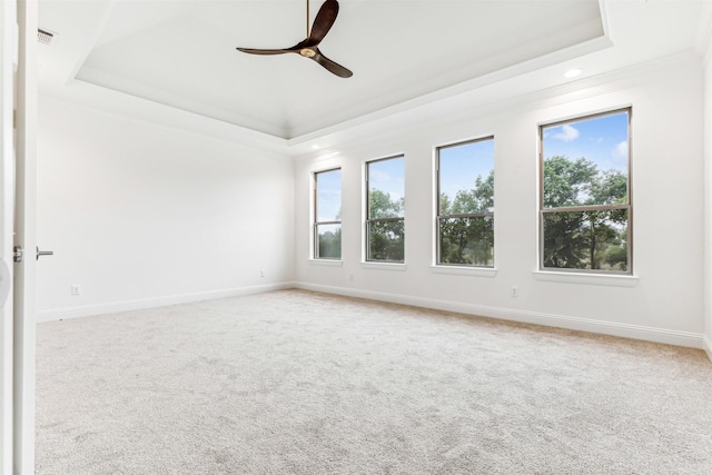 carpeted empty room with a ceiling fan, a tray ceiling, visible vents, and baseboards