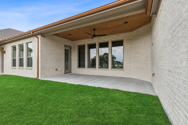 rear view of property with a ceiling fan, brick siding, a patio, and a lawn