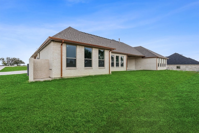 rear view of property featuring a shingled roof and a lawn