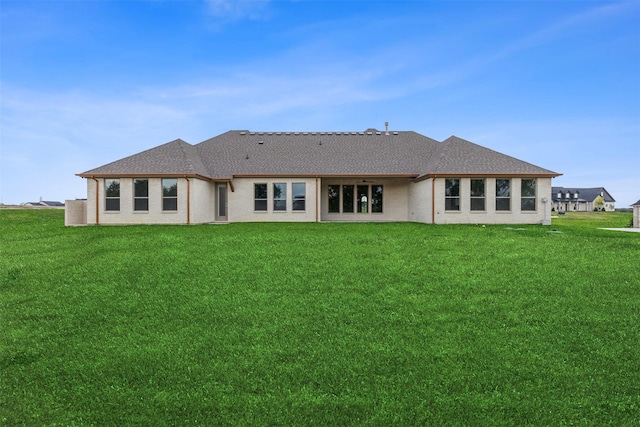 rear view of house with a shingled roof and a lawn