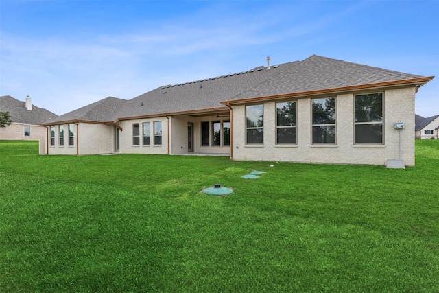 back of property with brick siding, a shingled roof, and a yard