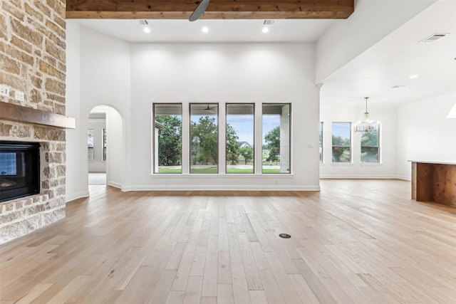 unfurnished living room featuring beamed ceiling, a high ceiling, a fireplace, and light hardwood / wood-style flooring