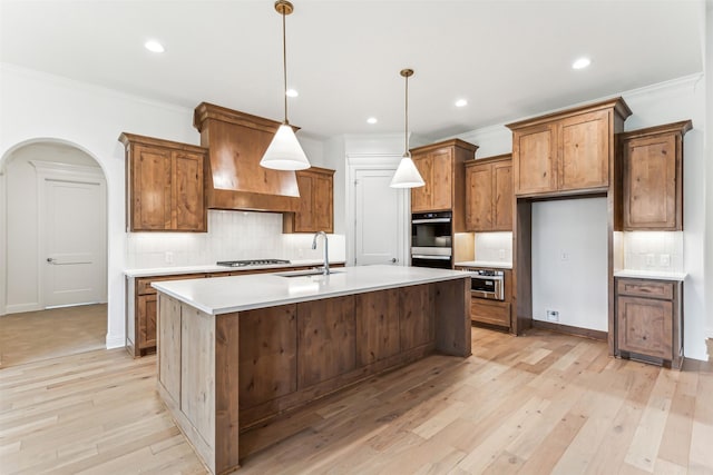 kitchen featuring arched walkways, stainless steel gas cooktop, premium range hood, a sink, and brown cabinetry