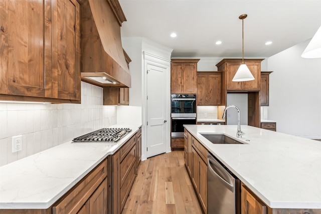 kitchen featuring decorative light fixtures, sink, stainless steel appliances, light stone countertops, and a center island with sink