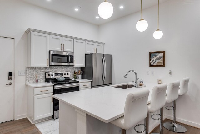 kitchen with pendant lighting, stainless steel appliances, sink, decorative backsplash, and white cabinets