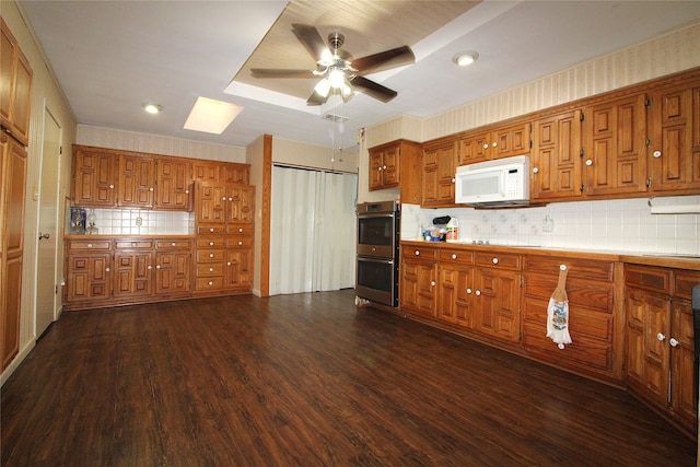 kitchen featuring black electric cooktop, dark wood-type flooring, stainless steel double oven, decorative backsplash, and ceiling fan