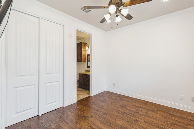 unfurnished bedroom with dark wood-type flooring, a closet, ceiling fan, and crown molding