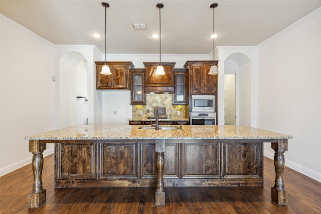 kitchen featuring a kitchen island with sink, dark hardwood / wood-style flooring, light stone counters, appliances with stainless steel finishes, and dark brown cabinetry