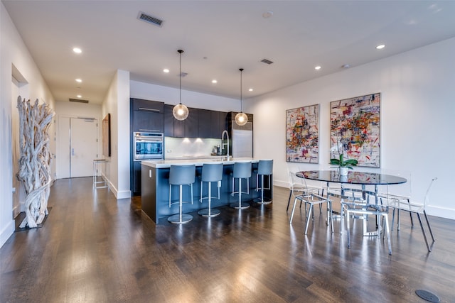 kitchen with backsplash, stainless steel oven, hanging light fixtures, dark hardwood / wood-style floors, and a kitchen island with sink